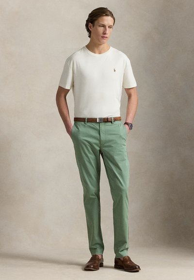 T-shirt branca de algodão com um pequeno logótipo, calças verdes de algodão, cinto castanho de pele e sapatos castanhos. Design simples e ajustado com textura lisa.