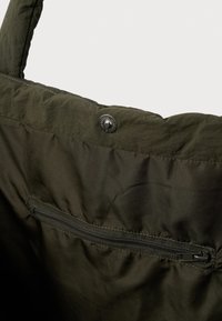 Σκούρο πράσινο υφασμάτινο σακίδιο με φερμουάρ εσωτερική τσέπη και μεταλλικό κουμπί σαγκρέ στο επάνω άκρο.