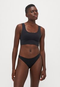 Svart bikini-sett med en bralette med firkantet hals og brede stropper, samt lavt midjebånd i thong-stil. Laget av glatt, elastisk stoff.
