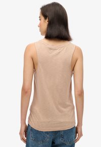 Camisa sin mangas de color beige claro con cuello redondo y textura suave, combinada con jeans de mezclilla de cintura alta. Vista trasera destacada.