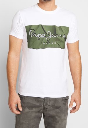 Hombre con camiseta blanca con el logo verde de "Pepe Jeans London" y pantalones de camuflaje grises, de pie con los brazos relajados a los lados.
