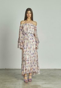 Blumiges, schulterfreies Maxikleid aus leichtem Stoff, mit Glockenärmeln, einer taillierten Silhouette mit einem lilafarbenen Gürtel und einem rüschengesäumten Saum. Lila High-Heels.