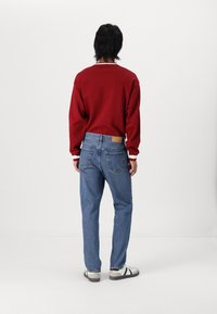 Red sweatshirt with contrasting white collar, paired with light blue denim jeans and white shoes with black stripes. Simple and casual design.