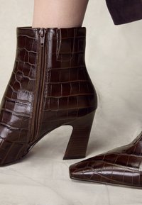 Braune Leder-Stiefeletten mit Krokodilprägung, spitzer Schuhspitze und einem Reißverschlussdetail an der Seite. Verfügt über einen Blockabsatz aus Holz.