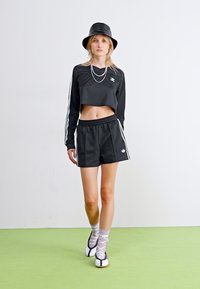 Svart cropped langermet skjorte og shorts, med hvite striper og logo. Kombinert med en svart bøttehatt og unike svart-hvite sko.