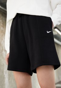 Černé šortky Nike vyrobené z jemné látky, se strečovým pasem, bočními kapsami a bílým logem na levé noze.
