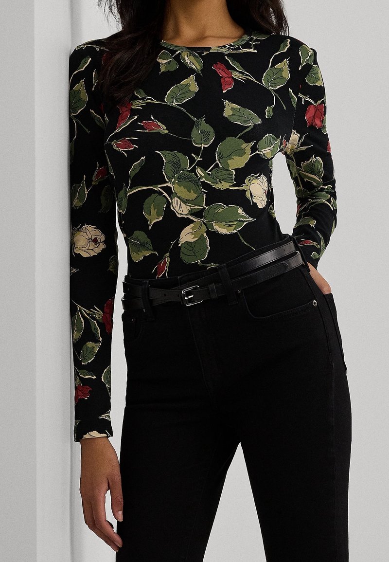 Haut à manches longues noir avec un motif floral rouge et vert, en tissu doux. Associé à un jean noir et une ceinture fine noire.