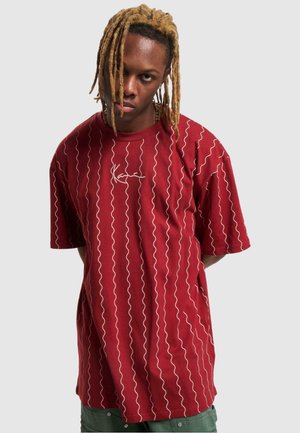 Rotes Baumwoll-T-Shirt mit weißem wellenförmigem Muster und kleinem Logo. Kurze Ärmel, Rundhalsausschnitt und entspannte Passform.