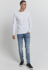 Vit långärmad t-shirt i bomull, ihopparad med ljusblå smala jeans. Skorna är svarta sneakers med vita sulor. Avslappnad stil.