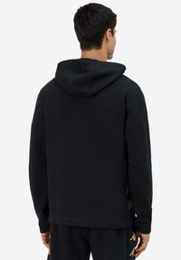 Felpa nera con tasca a canguro, cappuccio regolabile con cordino e dettagli dorati sui lati. Realizzata in un morbido tessuto testurizzato.