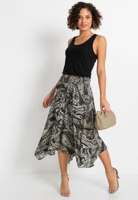 Top senza maniche nera abbinato a una gonna fluida nera e beige con motivo paisley, borsa a busta color nude e sandali beige con cinturini.