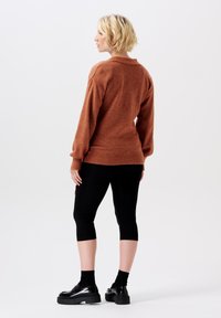 Rostfarbener Strickpullover mit lockerer Passform, gerippten Bündchen und Saum, kombiniert mit schwarzen, knöchellangen Leggings und klobigen schwarzen Schuhen.