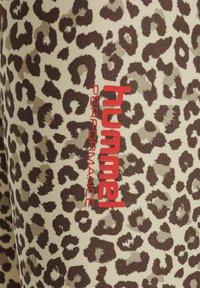 Leopardprint stof in tinten bruin en beige, met een rood "Hummel Performance" logo, benadrukt de textuur en het ontwerp van het materiaal.