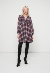 Καρό φόρεμα σε μπορντό και γκρι με ρίγες στον λαιμό και μακριά μανίκια. Φορεμένο με μαύρες καλσόν και ψηλοτάκουνα παπούτσια. Λείος υφασμάτινος χαρακτήρας.