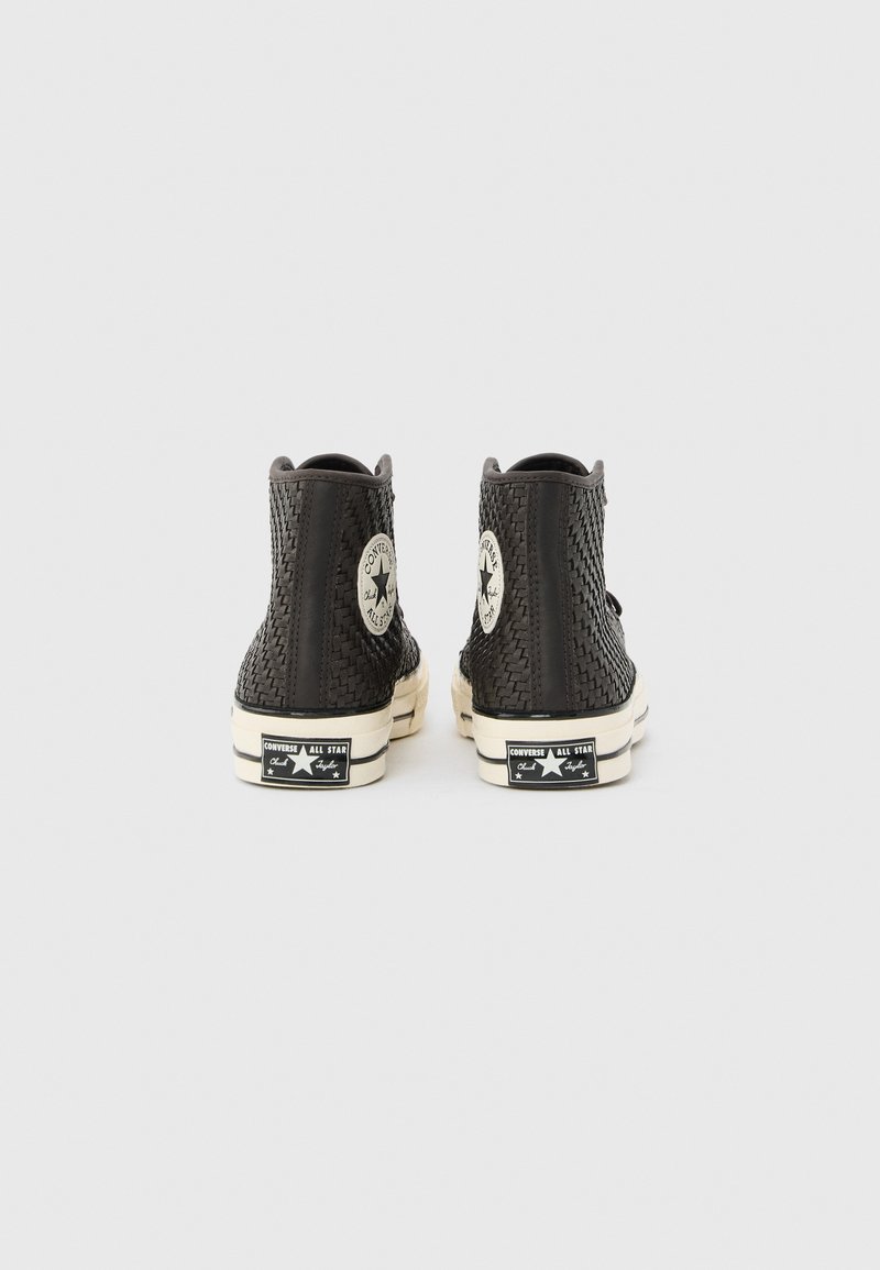 Black high-top Converse sneakers with woven texture, white soles, and iconic star logo on heel and ankle patch, viewed from the back.