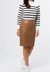 Jupe crayon en cuir marron associée à un pull rayé noir et blanc. Le mannequin porte des baskets blanches, affichant un look élégant et moderne.