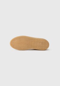 Semelle de chaussure en caoutchouc présentant une surface texturée et décorée de motifs, de couleur marron clair, avec un logo estampé près du talon.