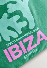 Groene katoenstof met abstracte vormen in lichtgroen, met de tekst "IBIZA" in vet roze, en "MEDITERRANEAN SEA" erboven.
