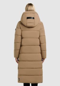 Lange pufferjas in beige met een aangesnoerde capuchon, verticale gestikte ontwerp, zwart logo detail op de achterkant en zijzakken.