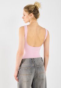 Body rosa chiaro senza maniche con scollo profondo sul retro, abbinato a jeans grigi sbiaditi a vita alta con due tasche posteriori.