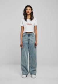 Hvit kort t-skjorte med rød og svart tekst "Niente," sammen med lyseblå vide jeans og hvite sneakers. Enkel, avslappet passform.