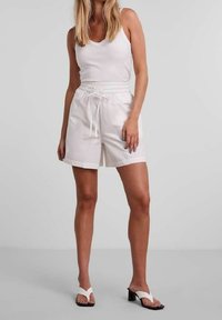 Bílé bavlněné šortky s elastickým pasem a šňůrkou, s bočními kapsami. Kombinované s bílým žebrovaným tílkem bez rukávů a sandály na podpatku.