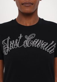 Juodas medvilninis marškinėlis su blizgančiu akmenukų dizainu kursyviu raštu per priekį. Trumpomis rankovėmis ir apvaliu kaklu.