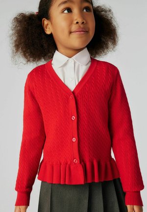 Red knitted cardigan with ribbed texture, V-neck, button closure, and peplum hem. Worn over a white collared shirt, featuring long sleeves.