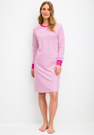 Femme debout pieds nus portant une robe longue aux genoux à manches longues rayée rose et blanche avec des poignets et un col rose vif.
