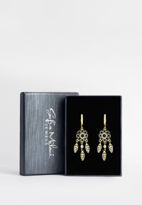 Guldtonade örhängen med cirkulära och bladdesigns, prydda med svarta och klara stenar, presenterade i en svart låda med texturerad yta.