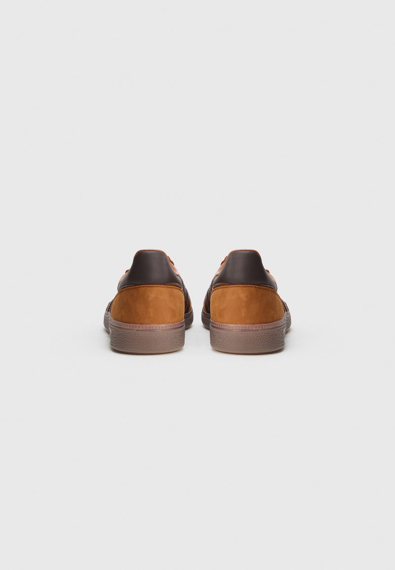 Brown leather and tan suede sneakers featuring a textured back, round heel, and minimalistic design. Flat rubber sole with subtle grip details.