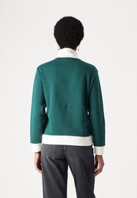 Sudadera verde con cuello y puños blancos, fabricada en una tela suave, con un corte relajado y sutiles detalles de costura en la parte trasera.