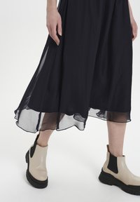 Black flowy dress with sheer hemline paired with beige ankle boots featuring a black elastic side panel and chunky rubber sole.