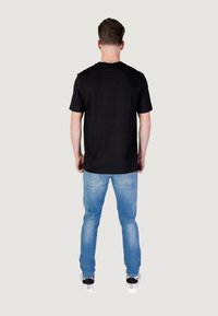 Zwarte korte mouwen t-shirt gecombineerd met lichtblauwe jeans. De jeans hebben een klassieke pasvorm met subtiele vervaging en een lichte verweerde textuur.