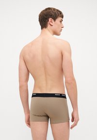 Braune Boxershorts mit schwarzem elastischem Bund mit "HUGO"-Markenlogo, von hinten an einem männlichen Modell gezeigt. Glatte Textur des Stoffes.