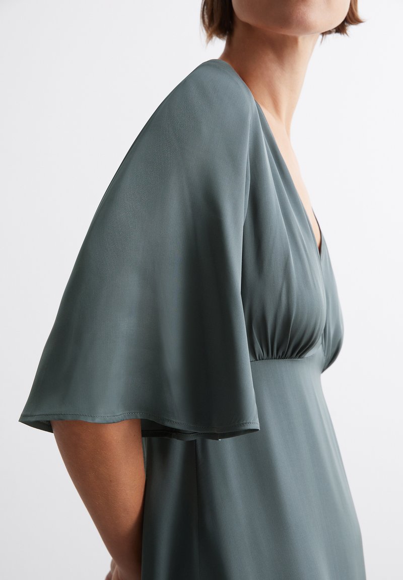 Leichtfallendes Kleid mit kurzen Ärmeln in sanftem Petrol, ausgestattet mit einem tiefen V-Ausschnitt, sanft gerafftem Taillenbereich und glattem, leichtem Stoff mit einem subtilen Glanz.