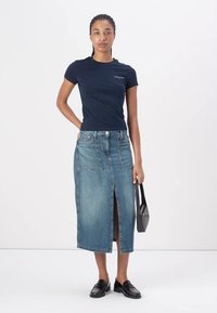 T-shirt a maniche corte blu navy abbinato a una gonna midi in denim blu con spacco frontale e tasche a toppa, accessorato con una borsa nera.