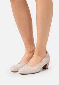 Ljust beige mockasklackar med rund tå och låg staplad klack, med en slät finish och subtil lyster.