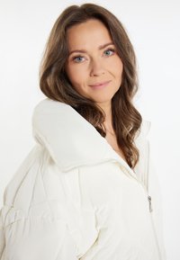 Jachetă puf albă cu guler înalt, design matlasat și fermoar frontal. Textură moale, netedă, cu detalii vizibile de cusut.