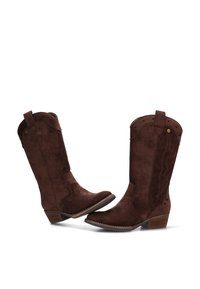 Par de botas de vaquero de ante marrón con tacones bajos apilados y costuras decorativas, posicionadas una frente a la otra sobre un fondo blanco.