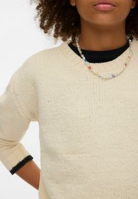 Suéter de punto color crema con mangas tres cuartos y acabado texturizado. Detalles acanalados en negro en los puños. Collar de cuentas con detalles coloridos.