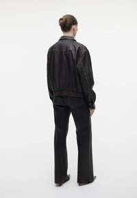 Zwarte leren bomberjack met elastische tailleband en manchetten, gecombineerd met zwarte flare-pantalon, die een soepele textuur en contrasterende stiksels toont.