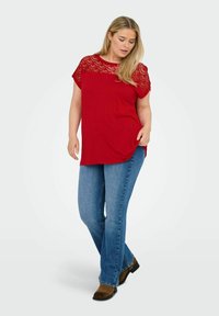 Rød T-shirt med kortærmer og struktureret blondeoverflade, parret med lyseblå jeans og brune ankelstøvler, i en afslappet pasform.