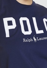 Námorně modré bavlněné tričko s velkým bílým nápisem "POLO" a textem "Ralph Lauren" pod ním, s vyšitým logem hráče póla.