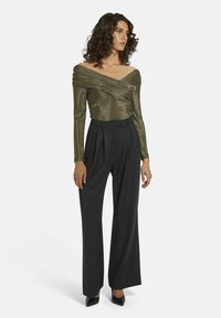 Schulterfreies, metallisch goldenes Oberteil aus strukturiertem Stoff, kombiniert mit hochtaillierten, weiten schwarzen Hosen und eleganten schwarzen Pumps.