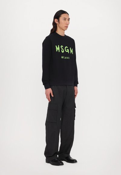 Zwarte sweatshirt met felgroene "MSGM MILANO" bedrukking, gecombineerd met donkere cargobroek. Gladde textuur, ronde halslijn, relaxte pasvorm.