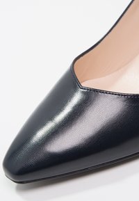 Chaussure à talon haut en cuir noir à bout pointu, texture lisse et doublure intérieure beige.