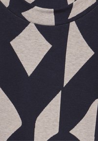 T-shirt textile avec une base bleu marine ornée d'un motif losange crème, col rond et texture douce.