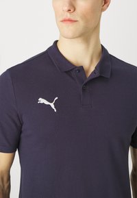 Marineblaues Poloshirt aus Baumwolle mit klassischem Kragen, kurzen Ärmeln und einem weißen, links auf der Brust gestickten Puma-Logo.