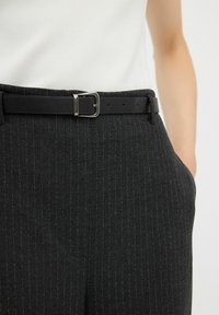 Svarta rutiga byxor med en slät textur, ett standardbälte med en silverfärgad spänne och sidofickor för praktisk användning.
